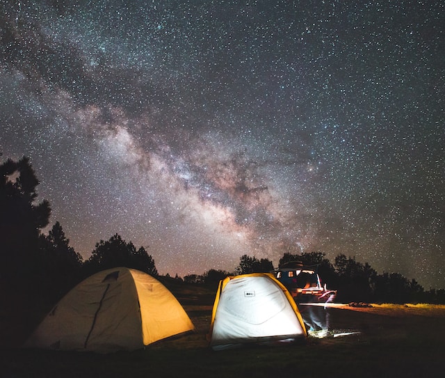 Camping tents set up on a filed with a view of the Milky Way above.
