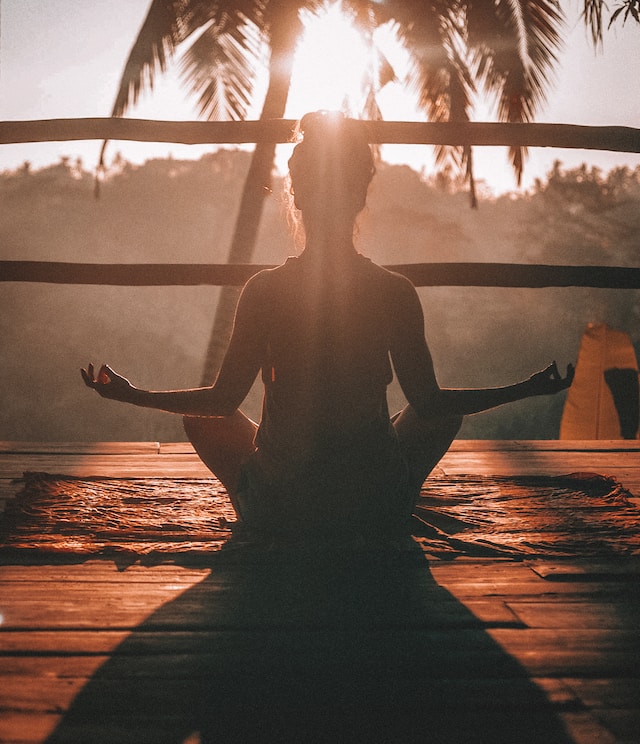 A woman meditates while facing the sun.