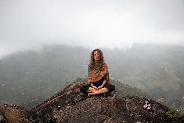 A woman sits with her legs crossed on top on a mountain.