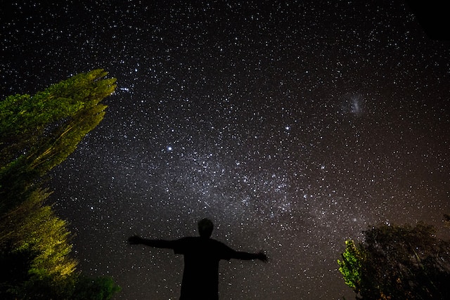 Silhouette of a person with outstretched hands looking up at the night sky