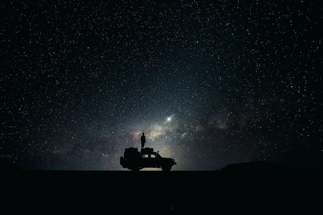 Silhouette of a person on top of a vehicle, looking up at a starlit sky
