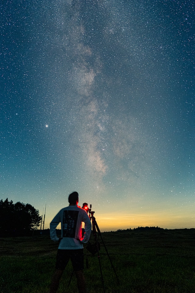A guy with a camera on a field, gazing up at the starry skies at night